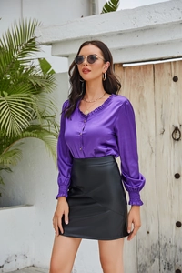Détail d'une jupe courte en similicuir noir mat portée avec un chemisier en satin violet