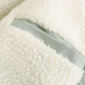 Gros plan sur la texture polaire crème et le tissu vert contrastant de cette parka d'hiver