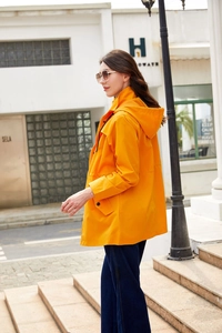 Detail eines orangefarbenen Trenchcoats mit Kapuze, Pattentaschen und Druckknöpfen