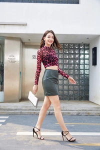 Detail of high-waist dark green PU leather mini skirt with side slit and slim fit cut