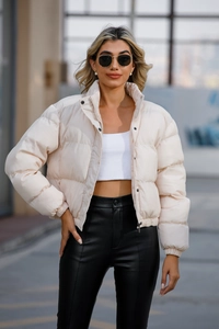 Detailed view of the stand-up collar and black snap buttons on cream puffer jacket