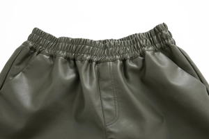Detailed close-up of high-waist elastic waistband on dark green faux leather shorts