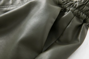 Detail of dark green PU leather shorts featuring side pockets and elastic pleated waistband