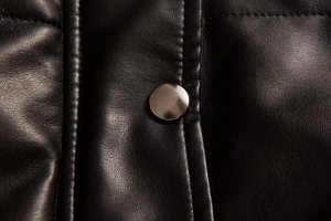 Detailed close-up of matte silver metal button and fine stitching on black faux leather vest