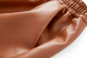 Detail of brown PU leather shorts showing elastic waistband and side pocket stitching