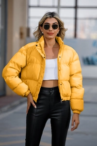 Detail of bright yellow short puffer jacket with high collar and black buttons for women