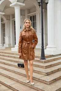 Scatto all'aperto di un trench lungo in pelle PU marrone con cintura e collo a revers