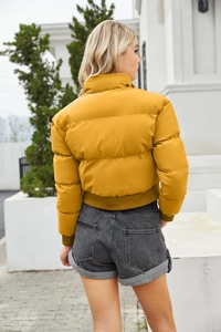 Back view of a cropped mustard yellow puffer jacket with casual grey denim shorts