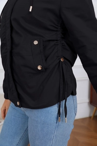 Detailed close-up of a women's black windbreaker featuring waist drawstrings and metal buttons