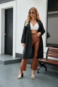 Detail van klassieke zwarte lange PU-lederen trenchcoat met top en bruine broek