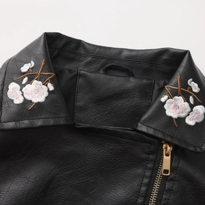 Detail of floral embroidery on black PU leather jacket with golden zipper closure