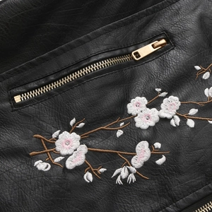 Close-up of floral embroidery and golden metal zipper on black pebbled leather jacket