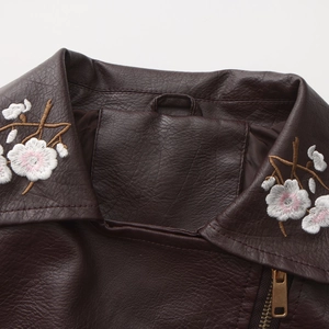 Close-up of white floral embroidery and gold zipper on a brown leather jacket lapel
