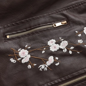 Macro detail of floral embroidery and gold zipper on a dark brown leather jacket