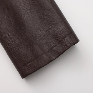 Detailed macro view of dark brown leather jacket hem with precise stitching on white background