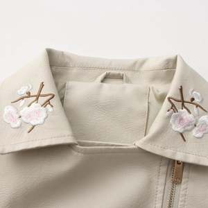 Close-up of floral embroidery on off-white leather jacket lapel with gold zipper detail