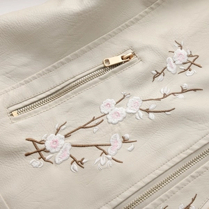 Detailed close-up of floral plum blossom embroidery on an off-white leather jacket zipper