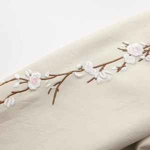 Close-up of floral embroidery on off-white faux leather jacket with detailed stitching
