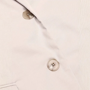 Detail of light beige vest featuring marble texture buttons and fine twill fabric texture