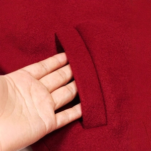 Close-up detail of burgundy wool jacket fabric with side pocket stitching and texture