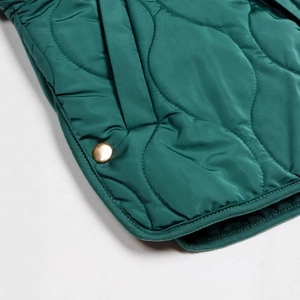 Detail der dunkelgrünen Steppjacke mit Wellennähten und goldenem Metalldruckknopf