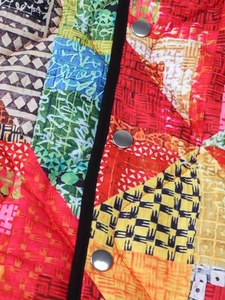 Detail of quilted patchwork jacket with colorful geometric prints and silver metal snaps