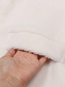 Detail der weichen weißen Kunstpelzjacke mit funktioneller Tasche und Plüschstruktur