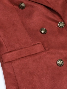 Detailed close-up of golden embossed heraldic buttons on a terracotta suede blazer