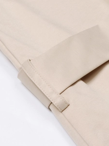 Détail du pantalon en sergé beige montrant les ourlets retroussés et les finitions soignées