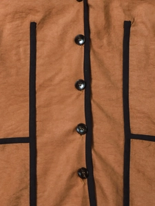 Detail of tan hooded jacket with marble pattern buttons and black decorative tape edges