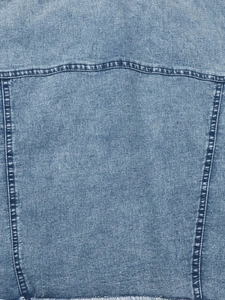 Detailed macro view of light blue denim jacket back with raw fringe hem and stitching