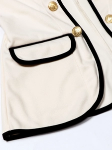 Detail of cream blazer showing black velvet trim and gold embossed badge buttons
