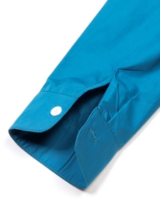 Vue détaillée du poignet d'une chemise bleu paon avec un bouton en résine blanche