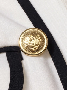 Close-up of golden embossed eagle button on white blazer with black trim detail