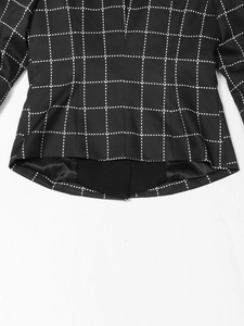 Detail of curved hem on black blazer featuring white houndstooth grid pattern and matte fabric