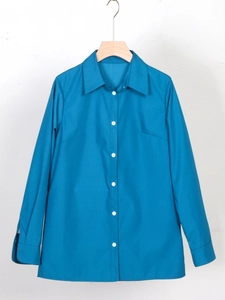 Chemise classique à manches longues bleu clair avec boutons blancs sur cintre en bois