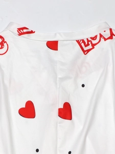 Close-up of white jumpsuit featuring red heart patterns and Love script print detail