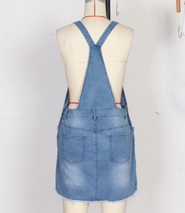 Detail view of denim overall dress showing Y-back straps and raw fringe hemline