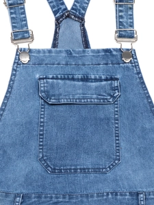 Detail of blue denim dungaree dress featuring a chest pocket and adjustable metal buckles