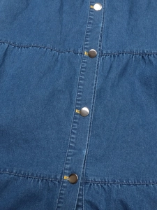 Détails d'une robe en jean bleu avec des boutons métalliques et des coutures jaunes