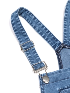 Detail view of washed blue denim overall dress with silver metal adjustable buckles
