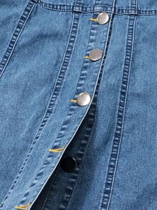 Detail eines blauen Jeanskleides mit silbernen Metallknöpfen und gelben Kontrastnähten