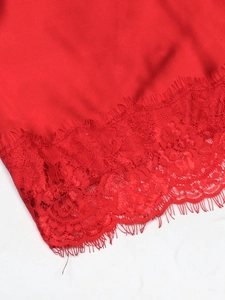 Detail of red silk slip dress showing the intricate eyelash lace hemline texture