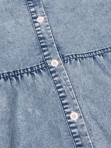 Detail of light blue denim dress showing white buttons and pleated sewing texture