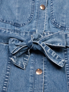 Dettaglio macro di un abito in denim con bottoni in metallo e fiocco in vita