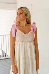 Détail des bretelles à nœuds roses et bustier froncé sur une robe longue crème