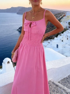 Abito rosa con spalline sottili, vita elasticizzata e fiocco su sfondo Santorini