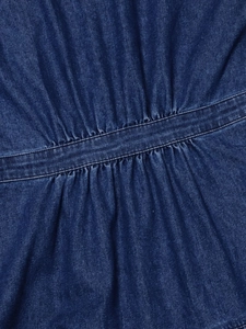 Dettaglio di abito in denim blu scuro con cuciture in vita a pieghe e trama