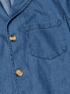 Détail de la robe en jean à col V montrant la poche plaquée et les boutons ambrés