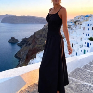 Elegant black smocked A-line maxi dress with bow detail against a sunset seaside background